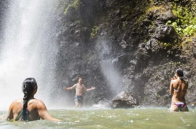 Swimmers standing waist-deep in the pool beneath a waterfall